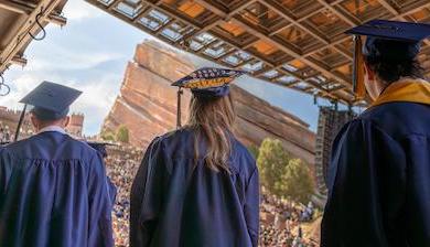 Three students in caps and gowns stand in line for their diploma at Red Rocks Amphitheatre.